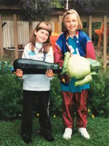 Two young girls, one holding a big zucchini, one holding a large cabbage.