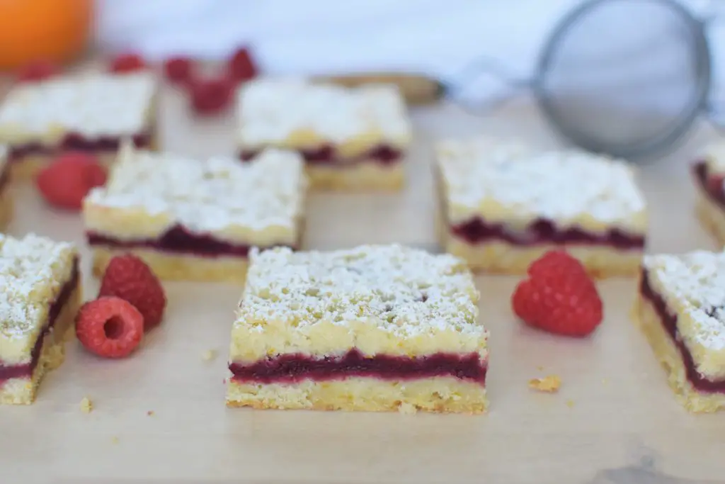 Raspberry orange shortbread bars laid out on parchment paper with raspberries - this bread will rise
