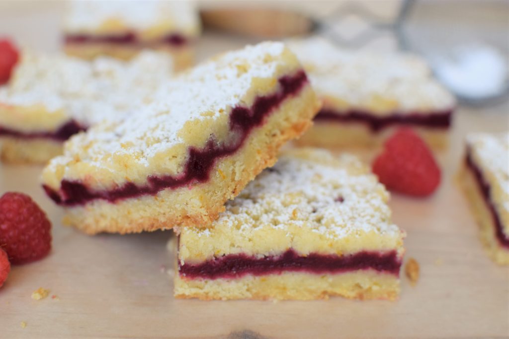 two raspberry orange shortbread bars laying against each other with raspberries around them