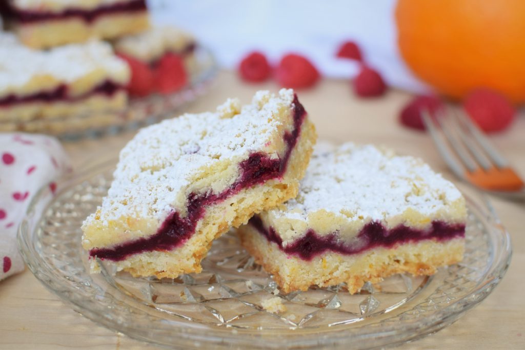 two raspberry orange shortbread bars on a cut glass plate - this bread will rise