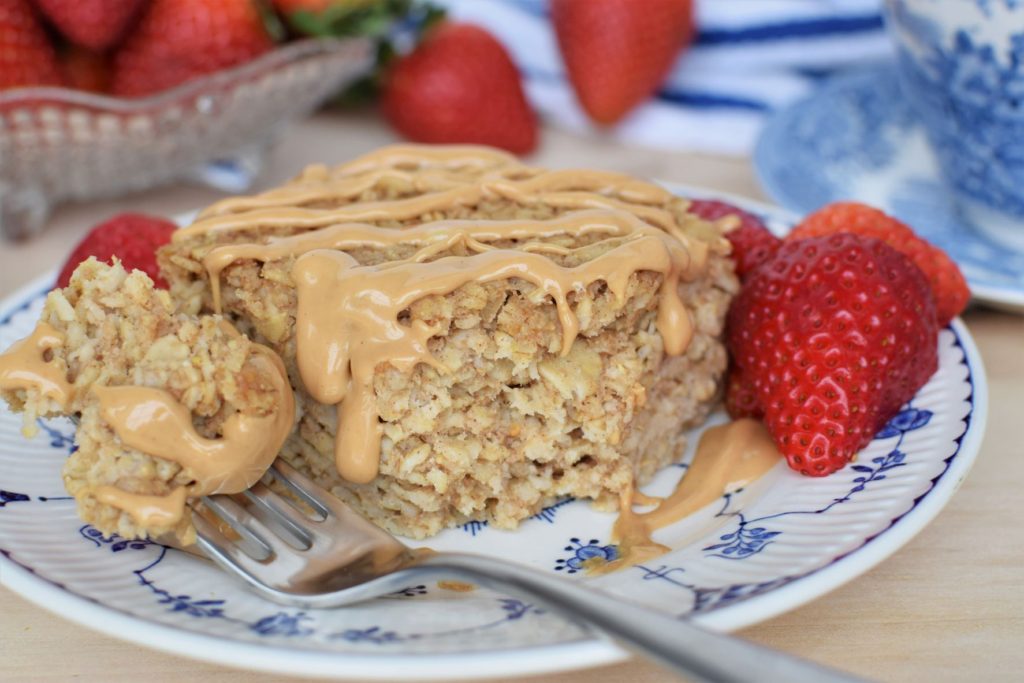 Baked oatmeal with cashew butter drizzle. Fork with bite on it.