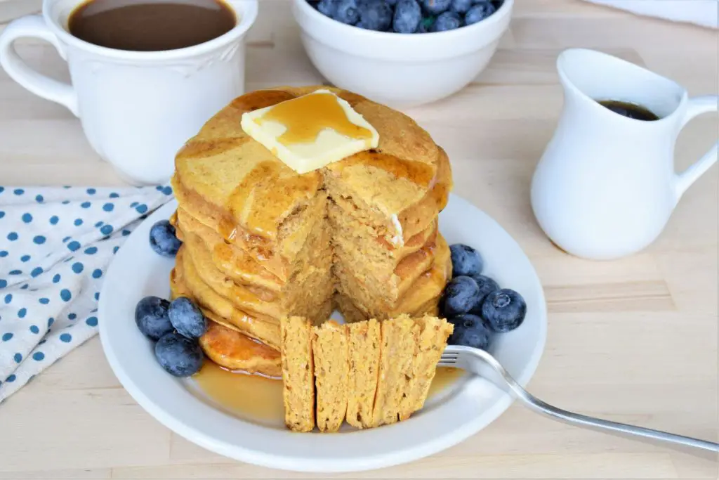 stack of butternut squash pancakes with butter and blueberries. Bite on a fork
