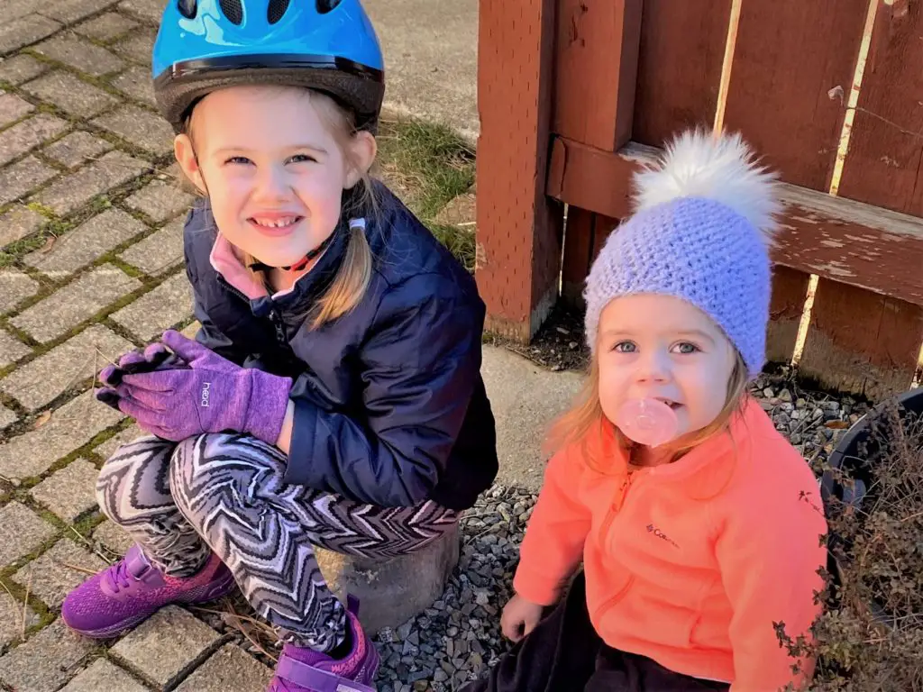 two girls sitting outside, one with bike helmet