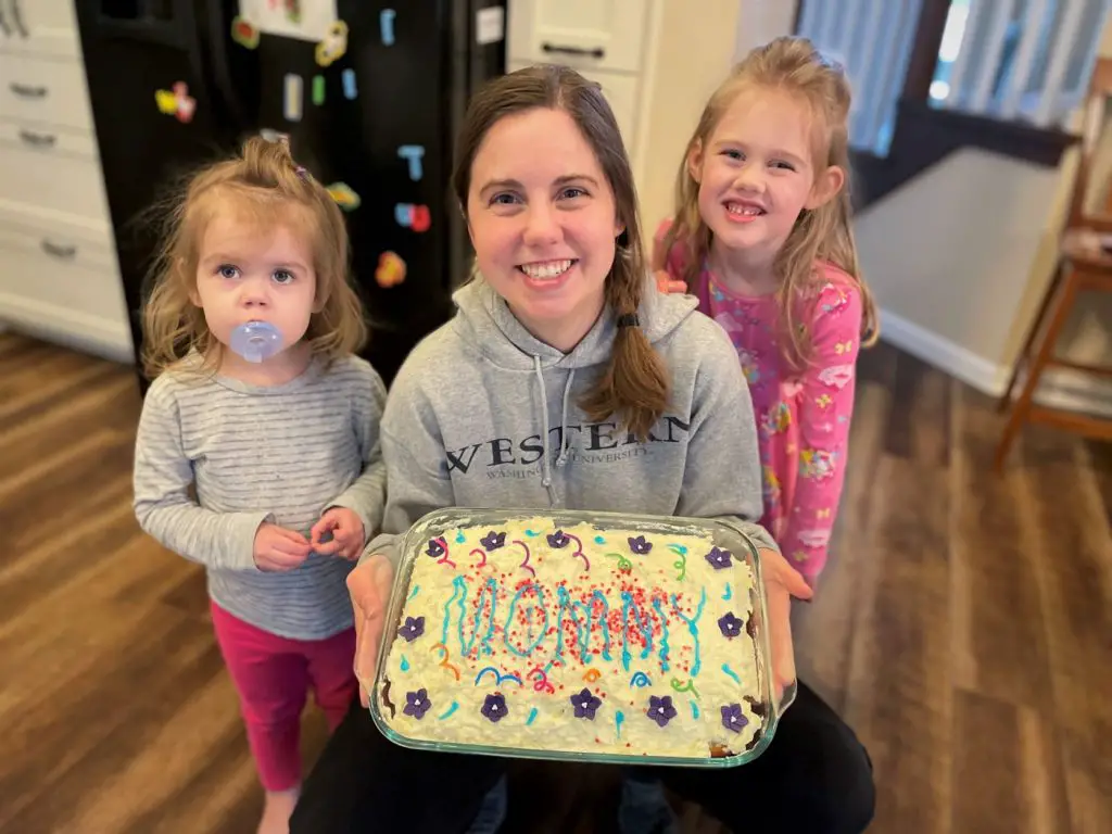 Two girls with mom holding birthday cake.