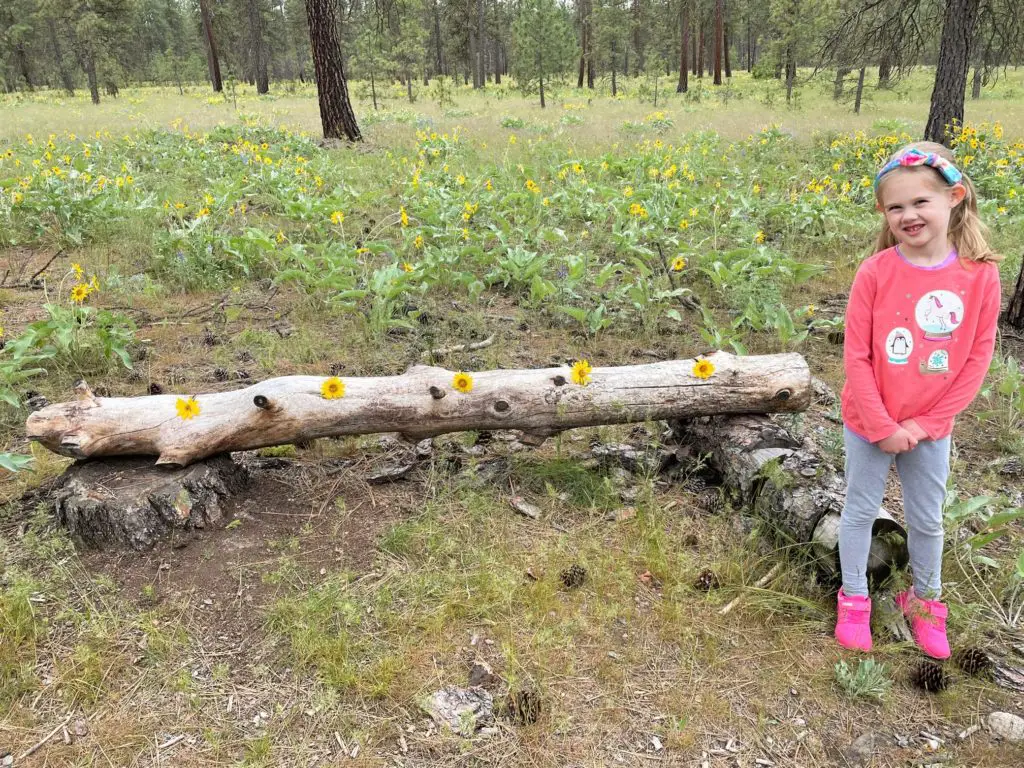girl standing next to log decorated in yellow flowers - this bread will rise