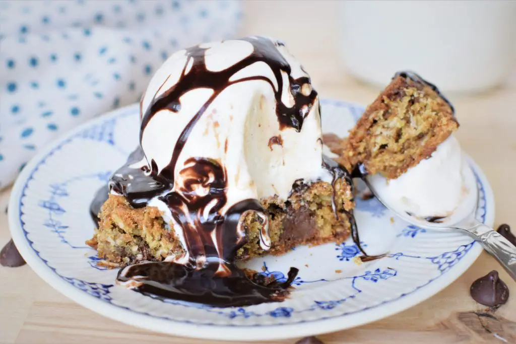 Bite taken out of oatmeal chocolate chip bar topped with ice cream and chocolate sauce.