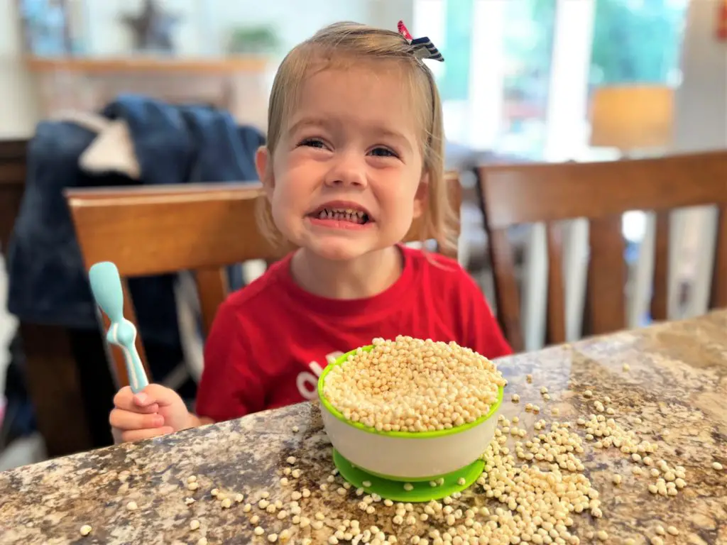 Young girl sitting at the counter with an overflowing bowl of millet puffs and a huge grin on her face - this bread will rise