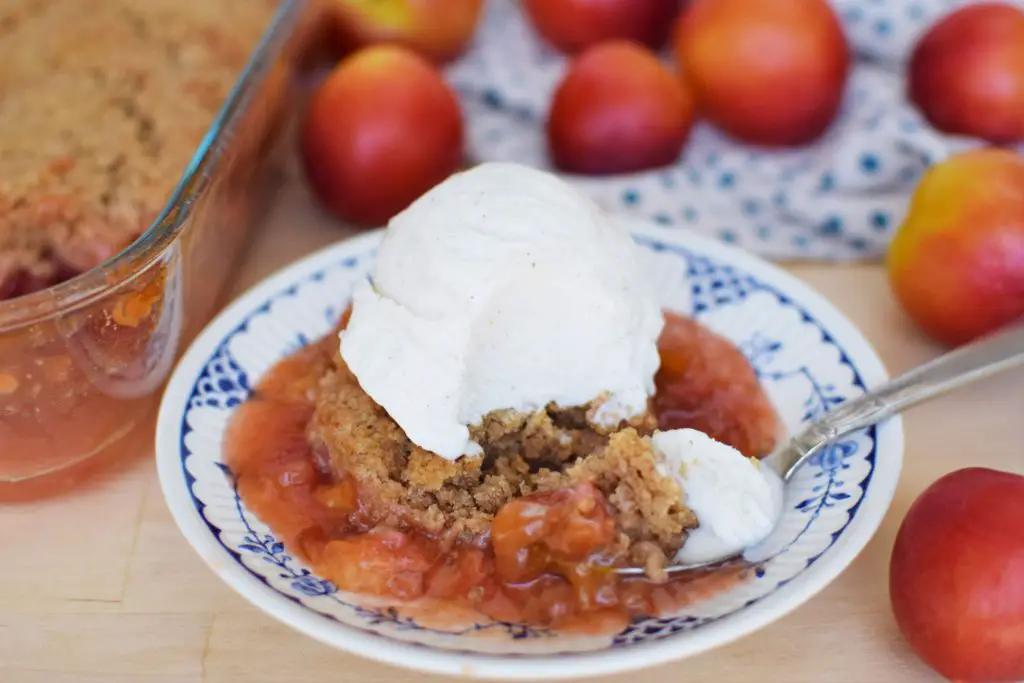 Bite on a spoon next to plum cobbler topped with ice cream.
