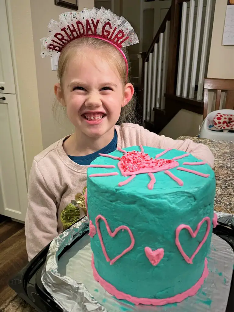 Girl with birthday headband with tall cake frosted in teal and pink.