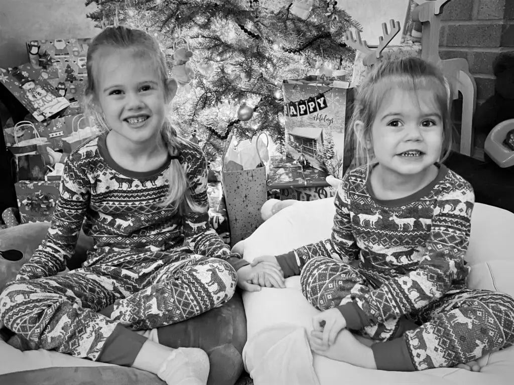 Two young girls in Christmas PJs in front of Christmas tree.