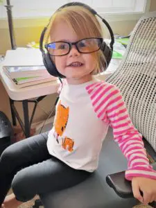 Young girl sitting at desk with headphones and glasses.