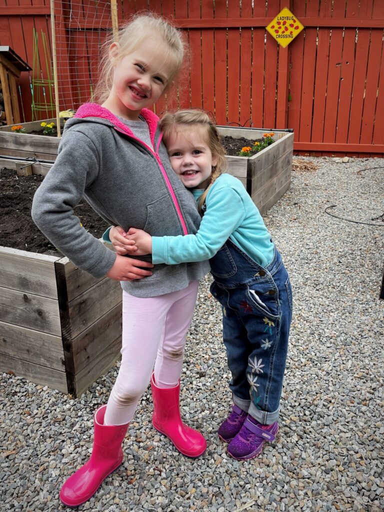 Two young girls hugging in the garden with overalls on - this bread will rise