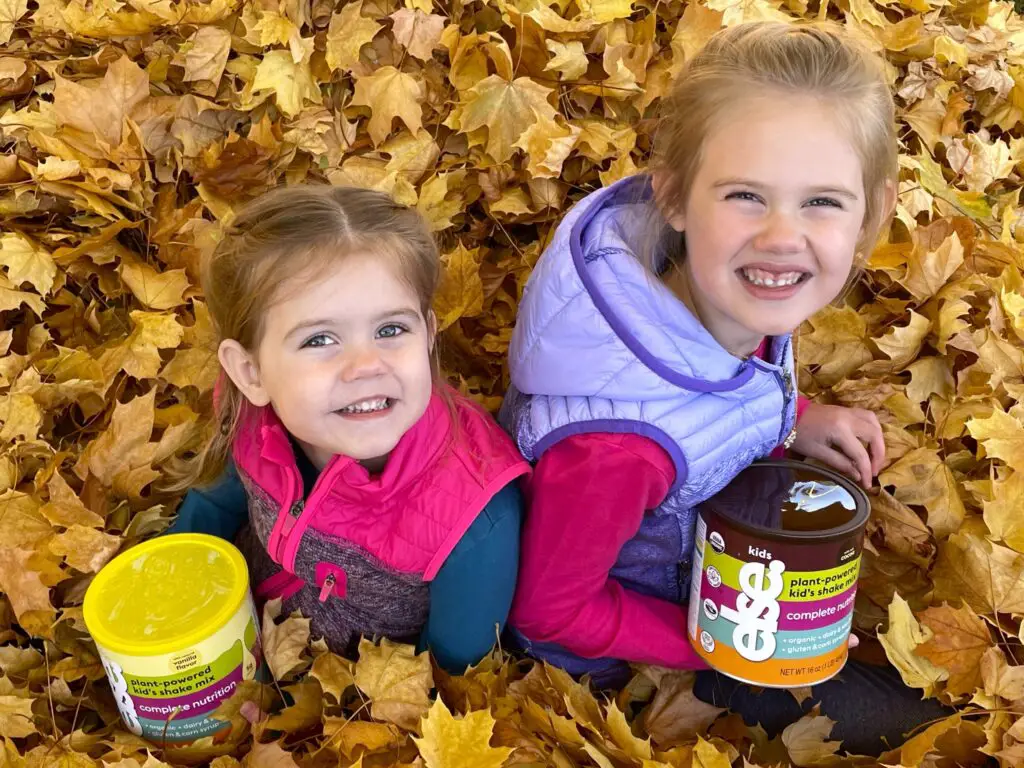 Two girls sitting in the leaves holding cans of formula - this bread will rise