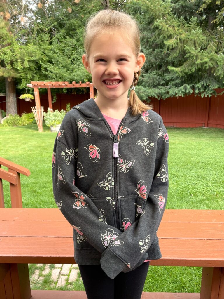 Rosie standing in backyard with butterfly sweatshirt on